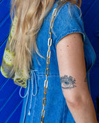 Close view of the flat gold-tone paperclip chain strap of a vintage brown alligator handbag worn over a blue denim dress.