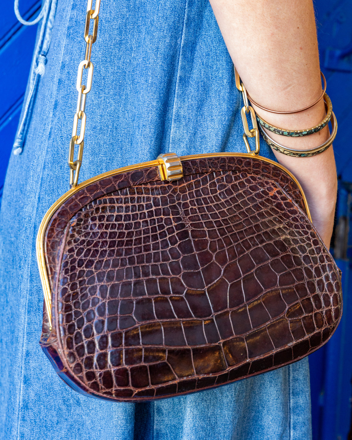 Close view of the front of a vintage brown alligator handbag showing the glossy scale pattern, polished gold-tone frame and fluted two-tone push clasp.