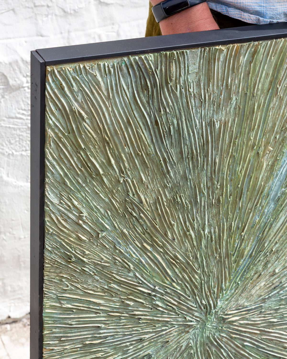 Top left corner of the painting against a white brick wall, showing the black frame and combed paint ridges.