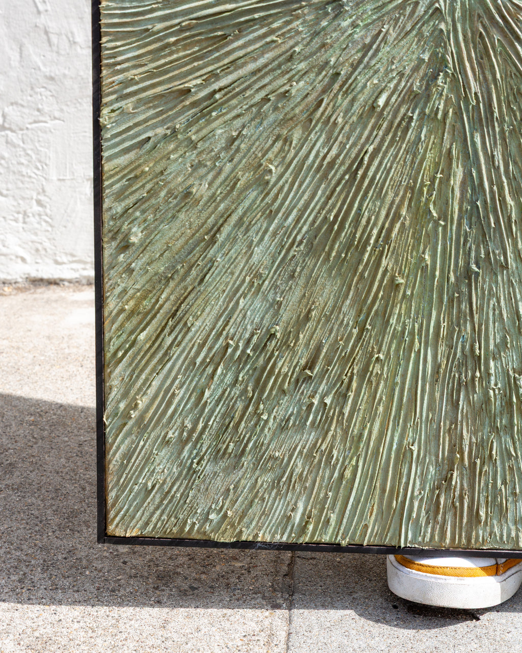 Bottom left corner of the painting resting on concrete, showing the frame edge and textured green paint.