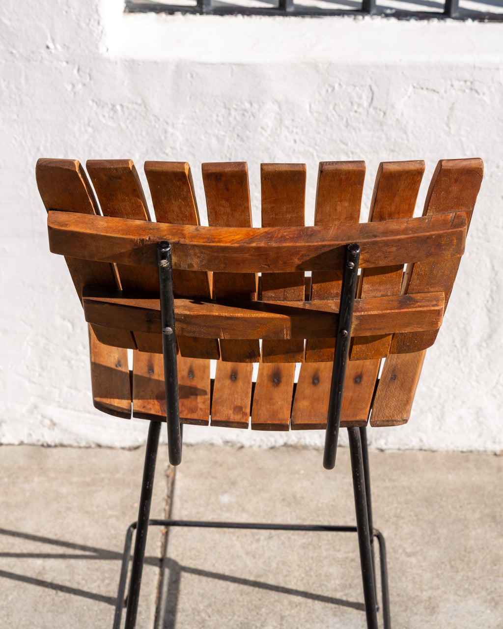 Back view of a slatted wood bar stool showing the two curved wood rails and black metal frame