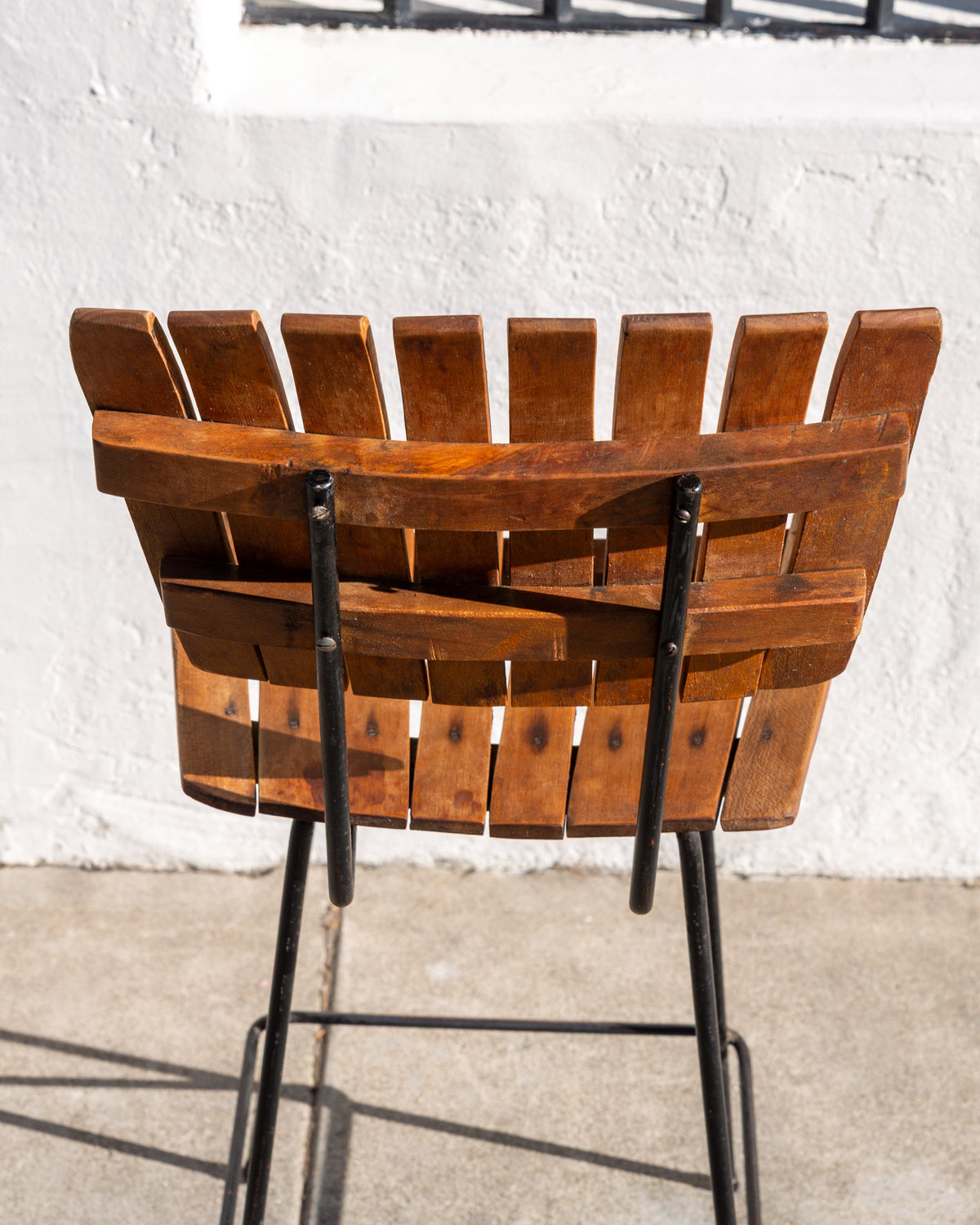 Back view of a slatted wood bar stool showing the two curved wood rails and black metal frame