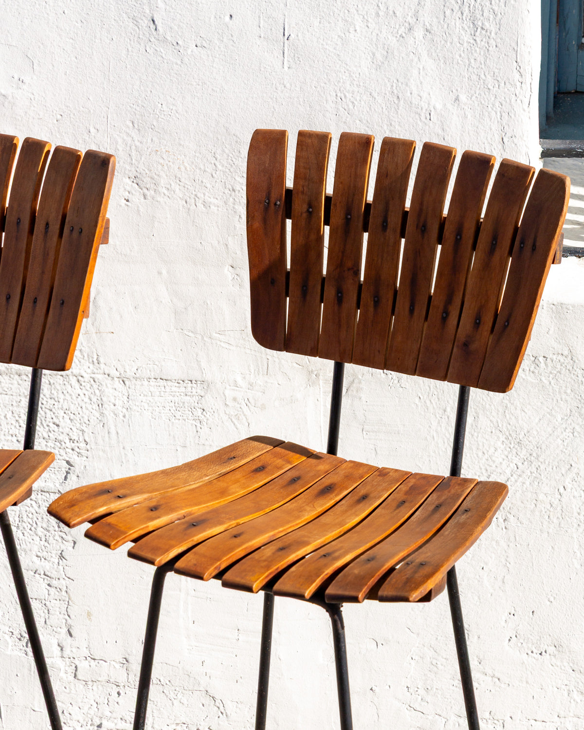 Two mid century bar stools side by side showing the curved slatted wood seats and backs