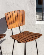 Close view of the slatted wood back and seat of a mid century bar stool on a black metal frame