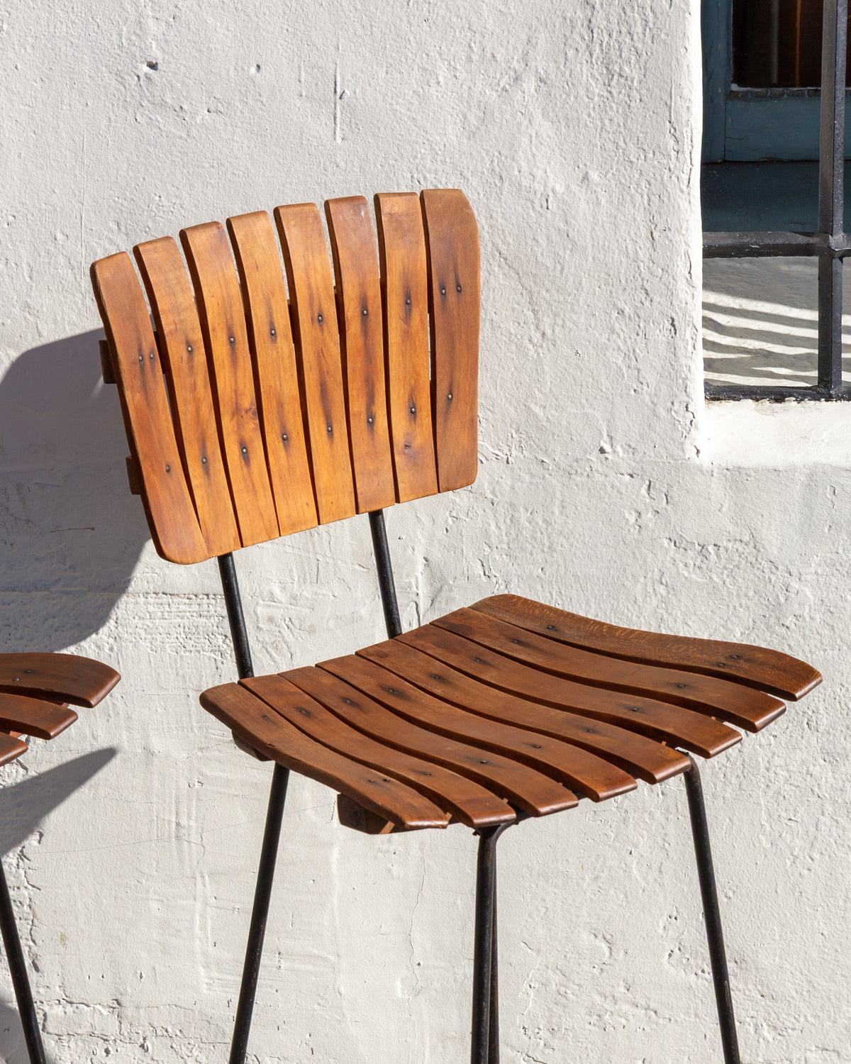 Close view of the slatted wood back and seat of a mid century bar stool on a black metal frame