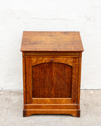 Front view of an antique tiger oak bin cabinet showing the arched tilt front panel and small turned wooden knob.