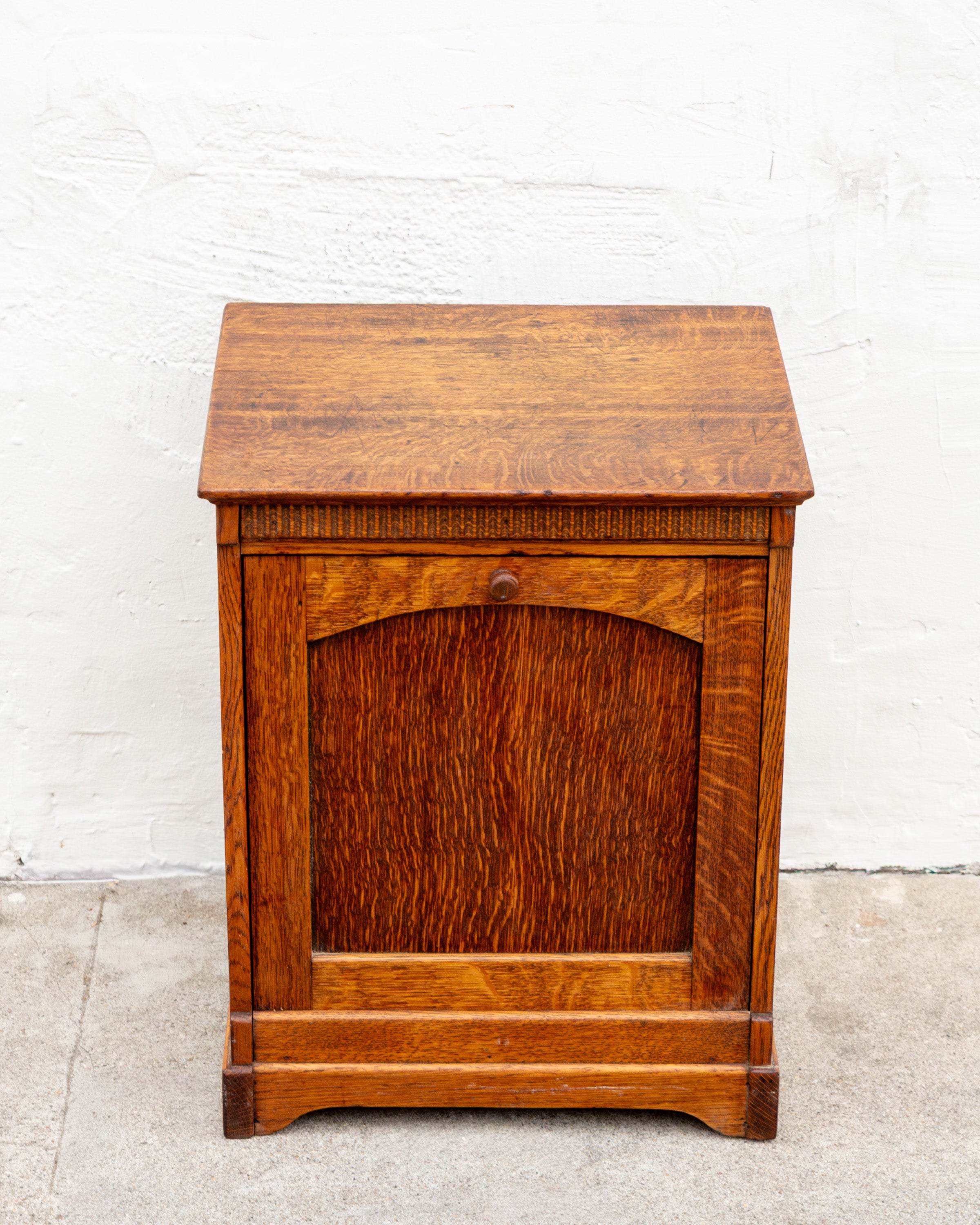Front view of an antique tiger oak bin cabinet showing the arched tilt front panel and small turned wooden knob.