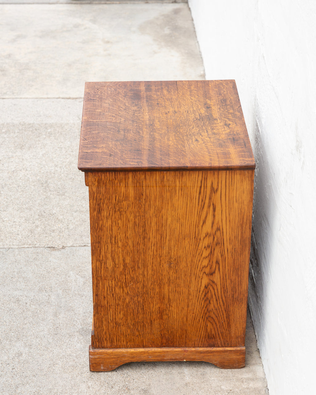 Side profile of an antique oak bin cabinet showing the heavily figured quarter-sawn side panel and molded base.