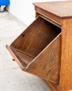 Side view of the antique oak cabinet with the tilt-out bin open, showing the sloped back of the compartment.