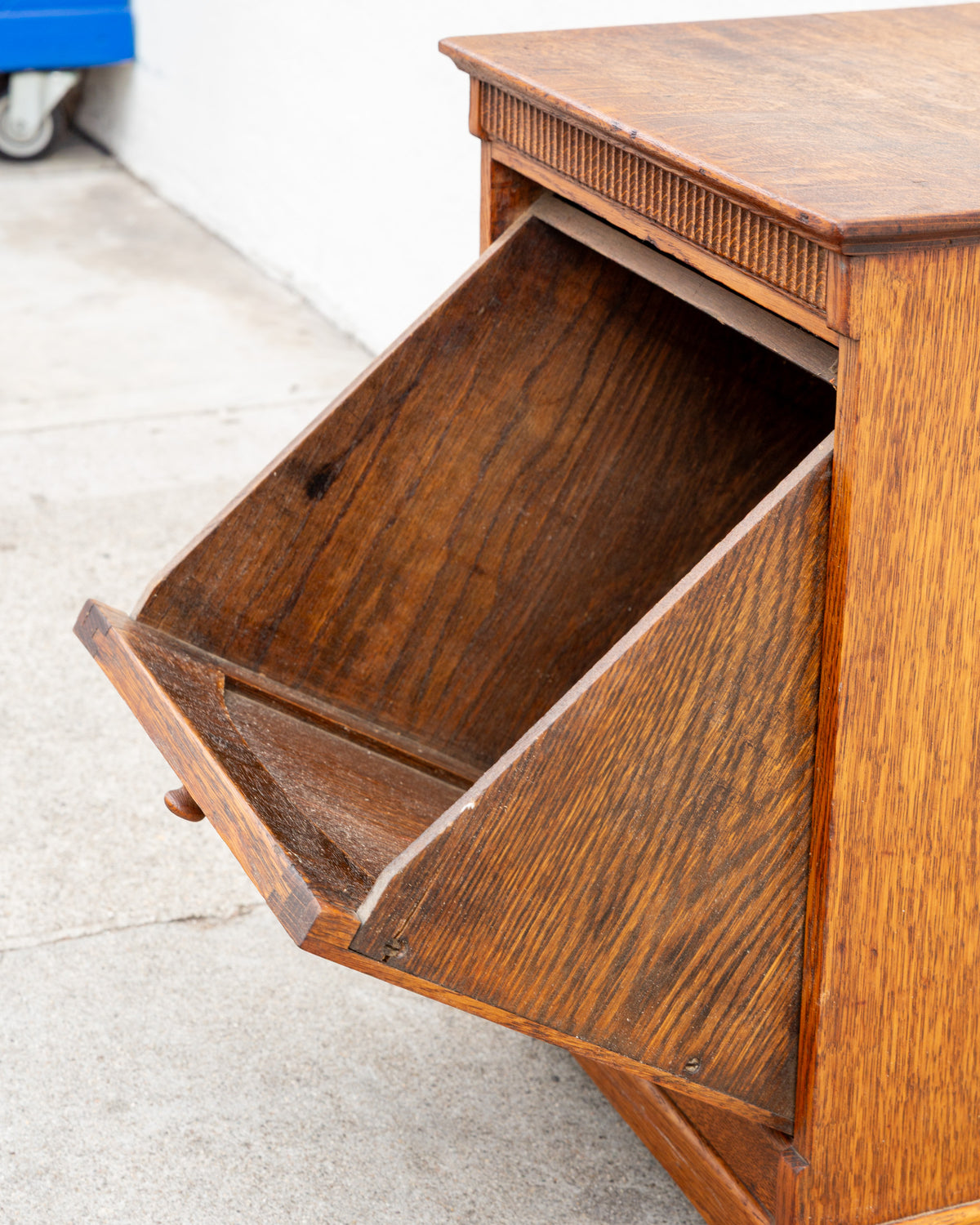 Side view of the antique oak cabinet with the tilt-out bin open, showing the sloped back of the compartment.