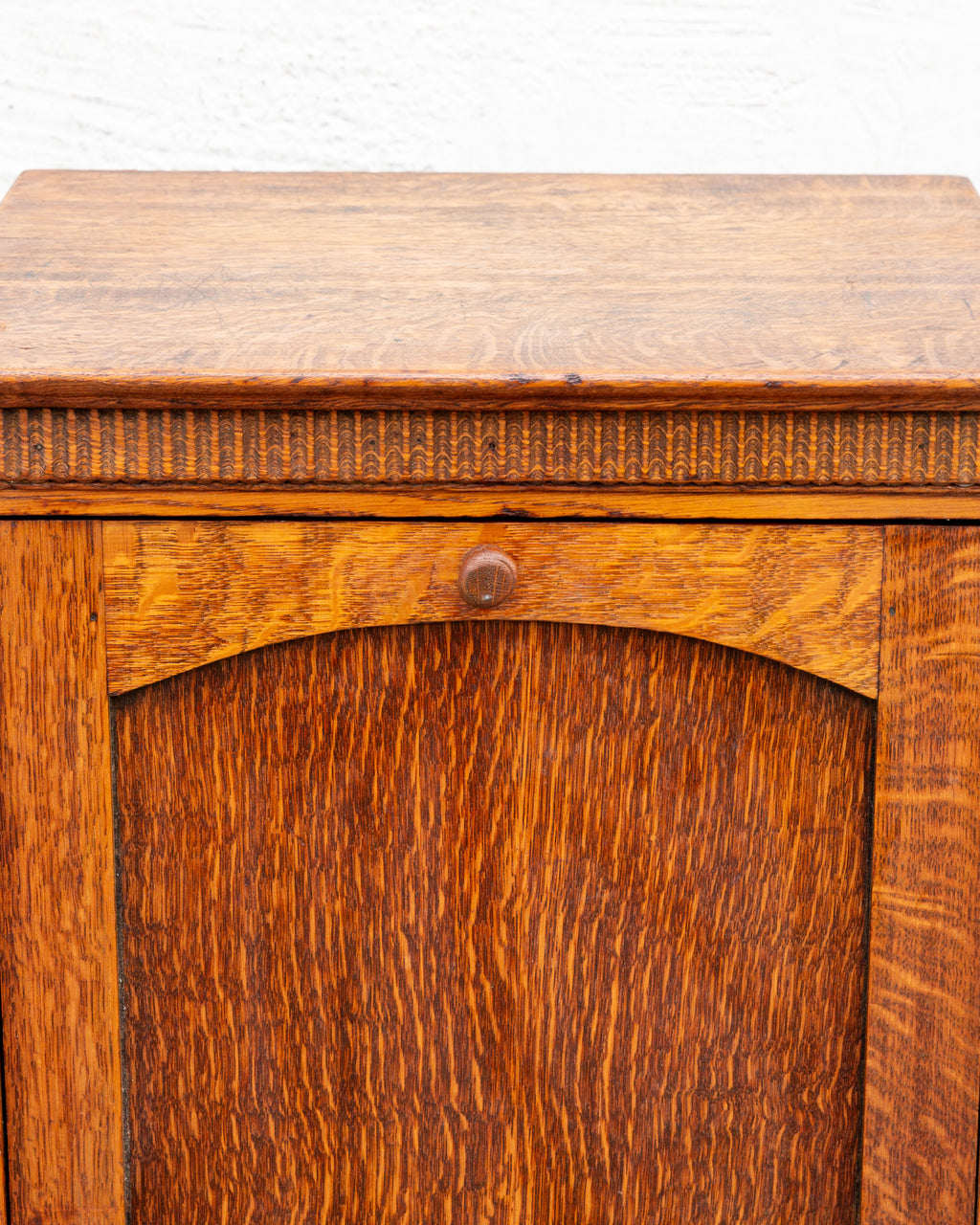 Detail of the oak cabinet showing the carved thumb molding beneath the top edge and the turned knob on the arched rail.