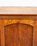 Detail of the oak cabinet showing the carved thumb molding beneath the top edge and the turned knob on the arched rail.