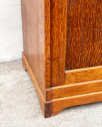 Detail of the lower corner of the oak cabinet showing the molded plinth, shaped bracket foot and pegged through-tenon.
