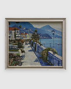 Palette knife painting of a Mediterranean lakeside promenade with villas and blue mountains in a white frame on a light gray background