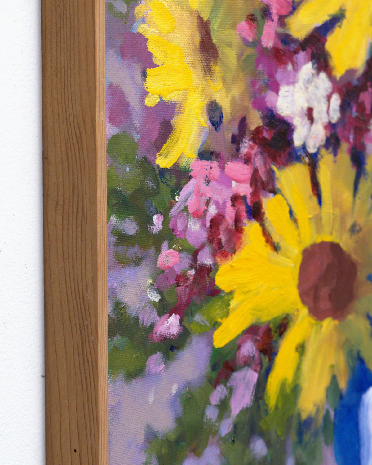 Side view of the natural wood strip frame on the floral still life painting, showing frame depth against a white wall.