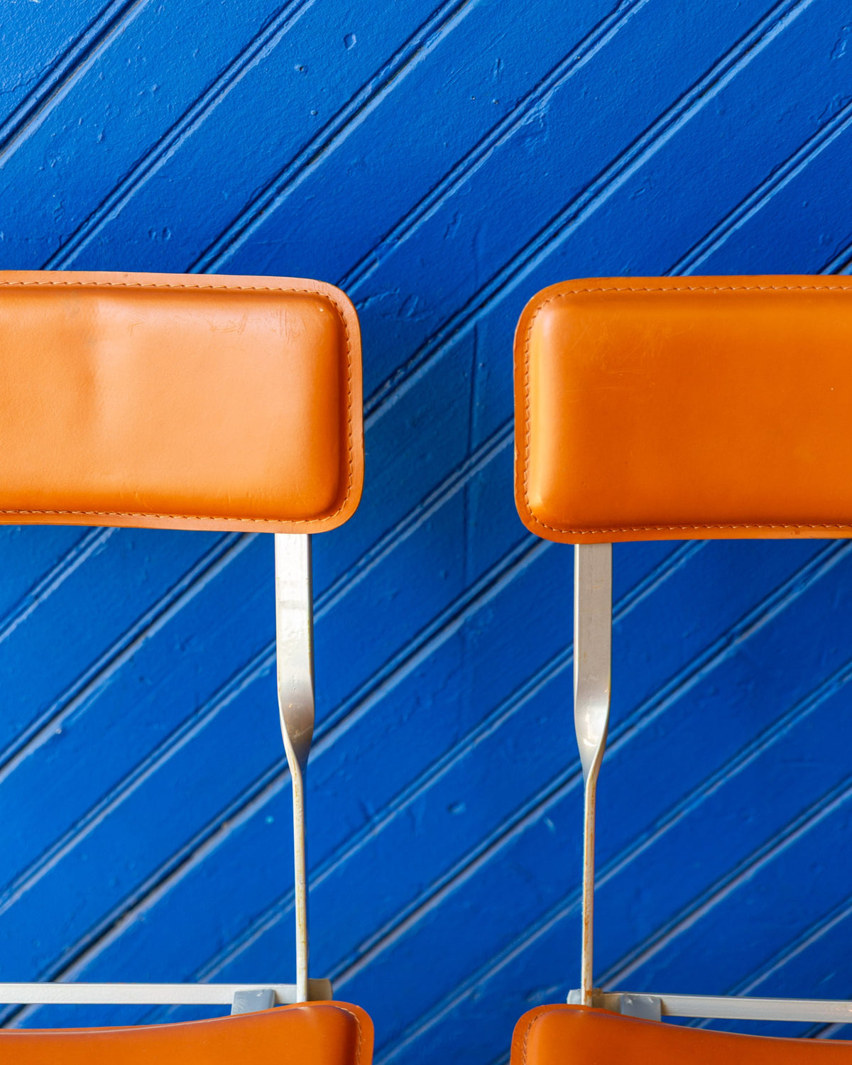 Close view of two cognac leather backrests with stitched borders on gray metal uprights.