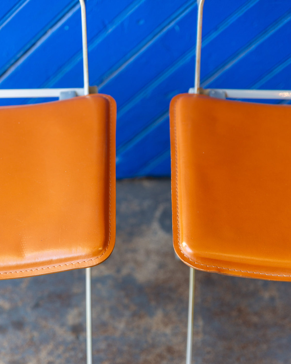 Front edges of two padded cognac leather folding chair seats.