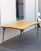Angled view from the opposite end of a freeform maple dining table with sculptural cast aluminum legs.