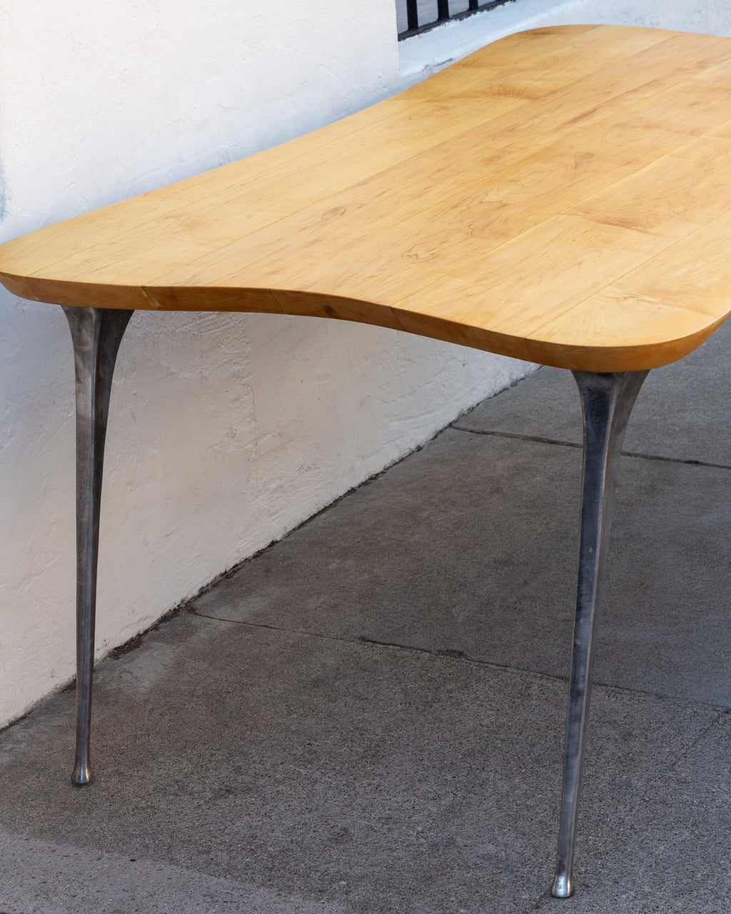 Side of a freeform maple tabletop showing the curved edge and two flared cast aluminum legs.