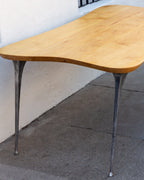 Side of a freeform maple tabletop showing the curved edge and two flared cast aluminum legs.
