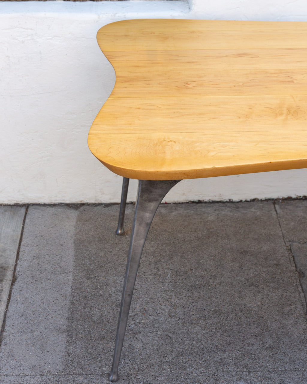 Rounded corner of a solid maple tabletop with its tapered cast aluminum leg and small rounded foot.
