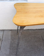 Rounded corner of a solid maple tabletop with its tapered cast aluminum leg and small rounded foot.