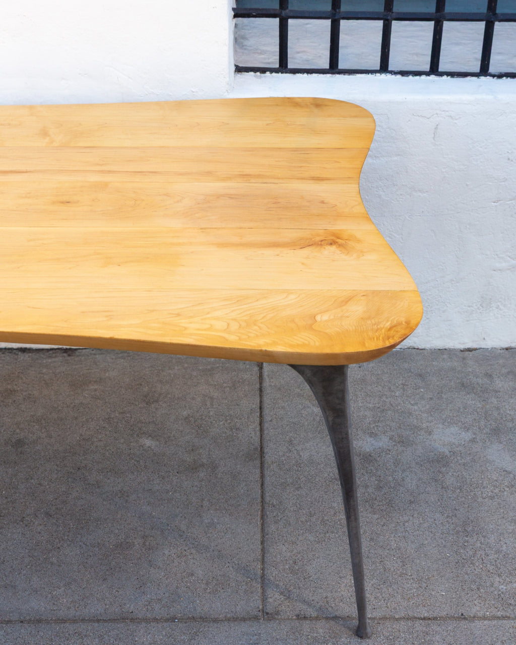 Second corner of a freeform maple table showing edge-joined boards and a cast aluminum leg.