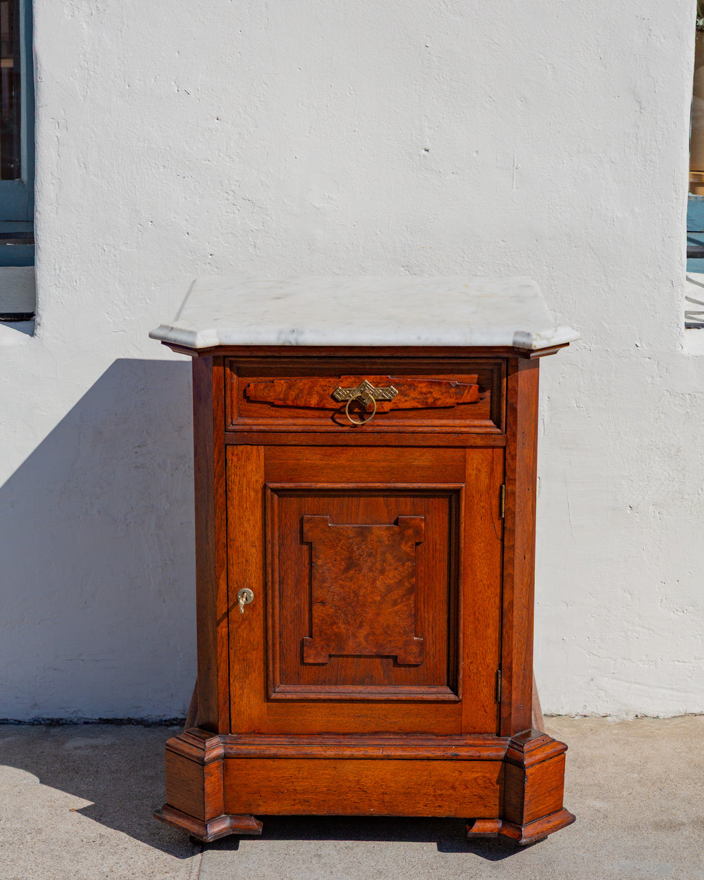 Straight-on front view of the Victorian marble top cabinet showing the burl walnut drawer panel, brass ring pull and paneled door