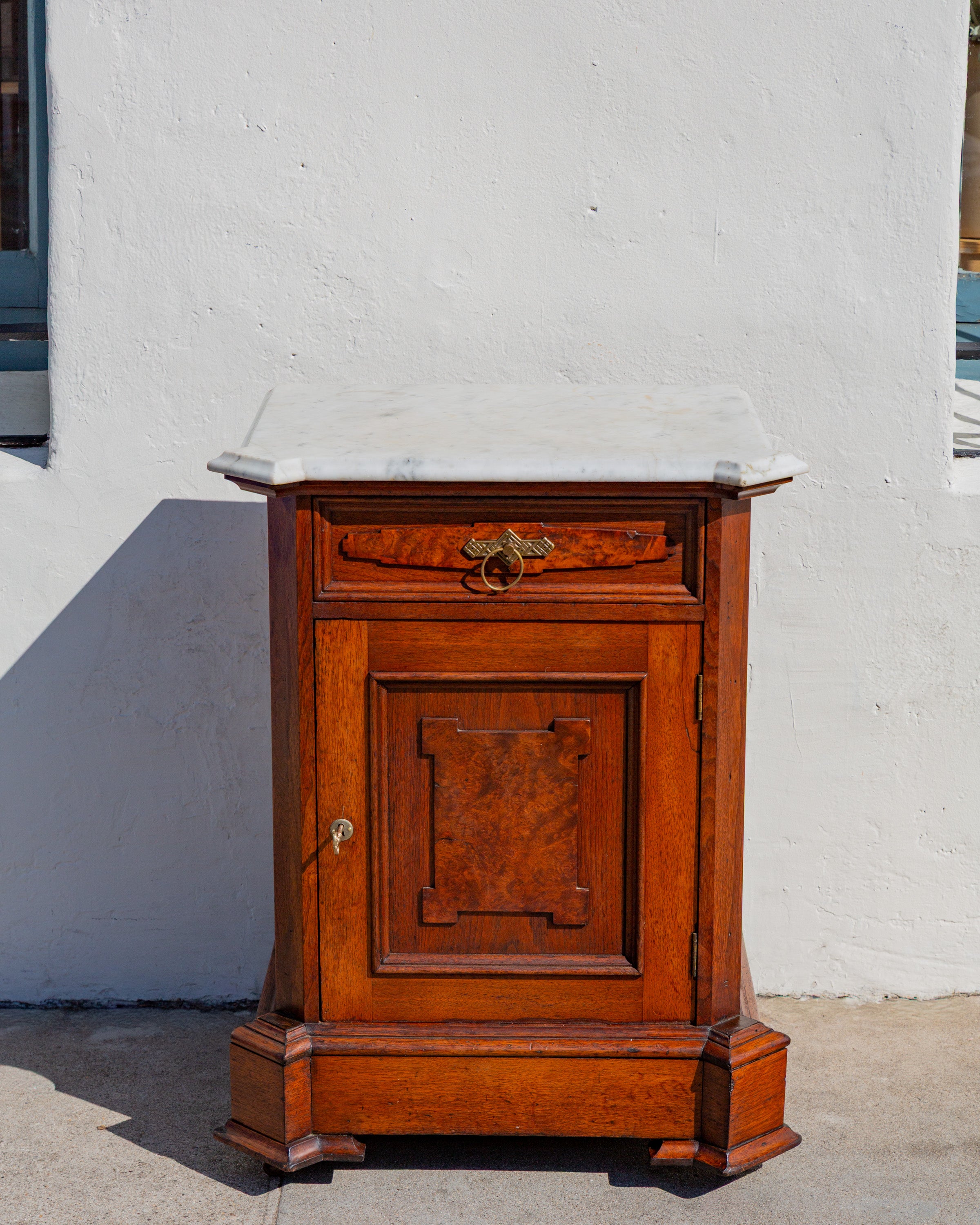 Straight-on front view of the Victorian marble top cabinet showing the burl walnut drawer panel, brass ring pull and paneled door