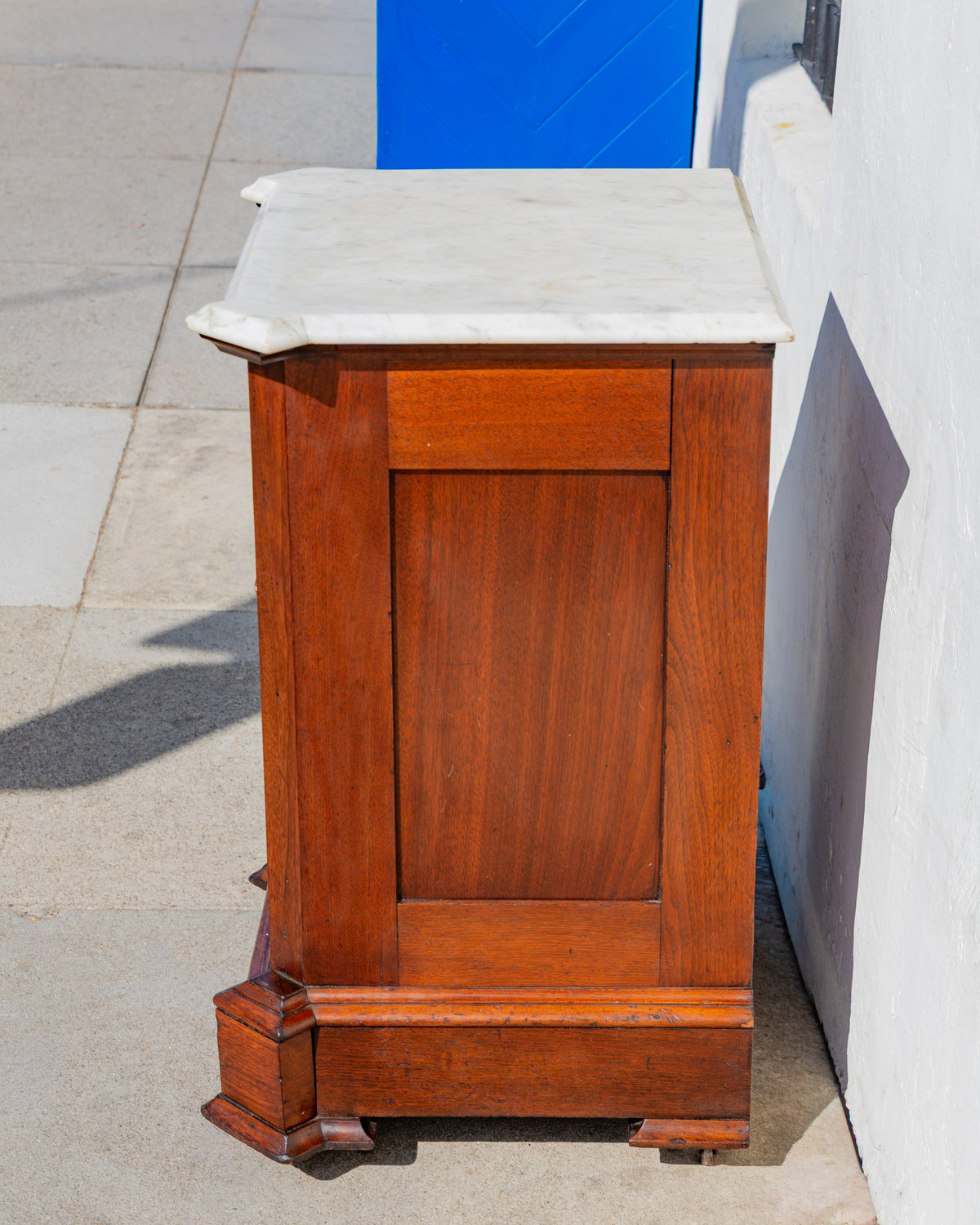 Side view of the walnut cabinet showing the recessed side panel and the molded edge of the marble top