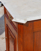 Detail of the canted corner of the white Carrara marble top above the burl drawer front and brass ring pull