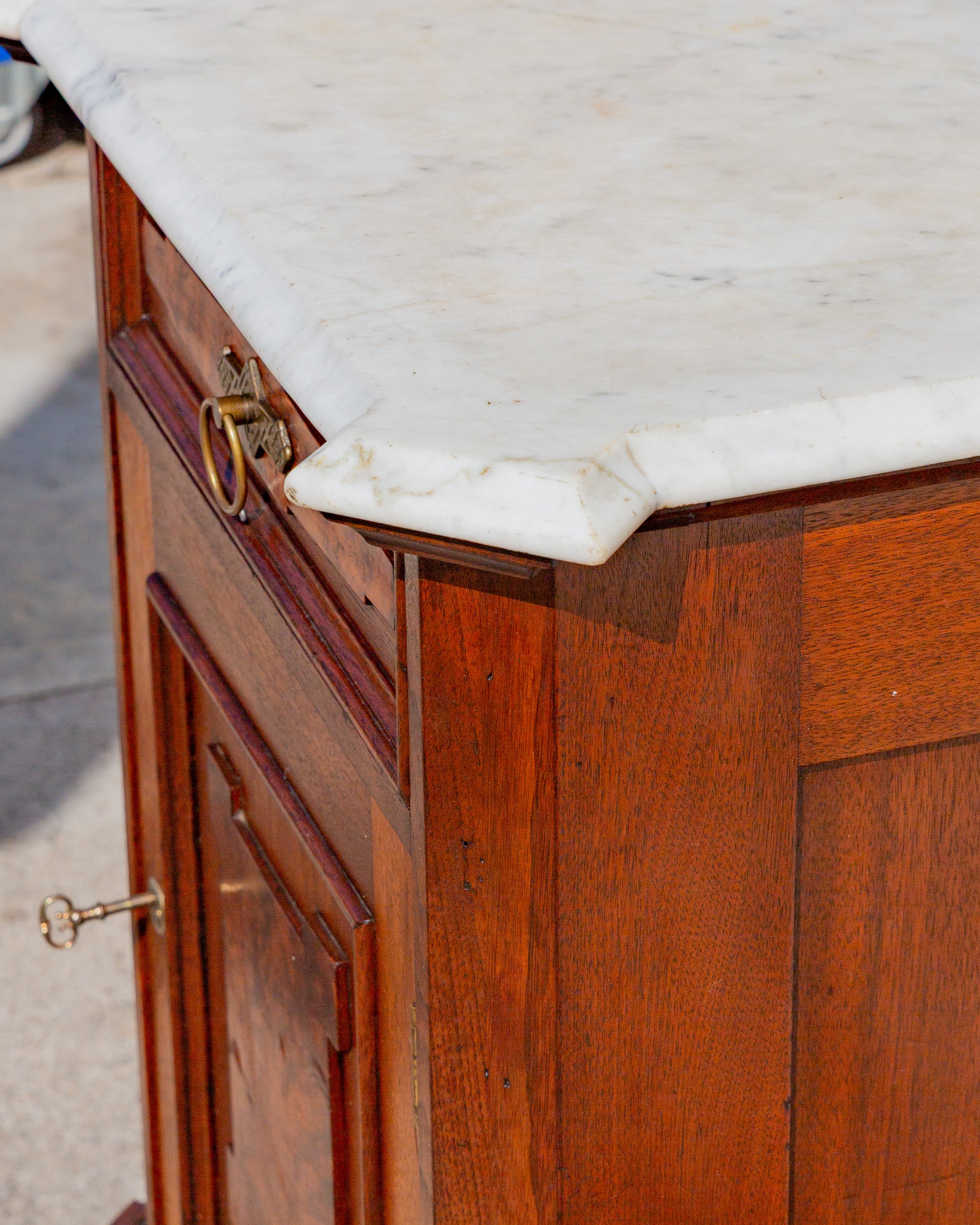 Detail of the canted corner of the white Carrara marble top above the burl drawer front and brass ring pull