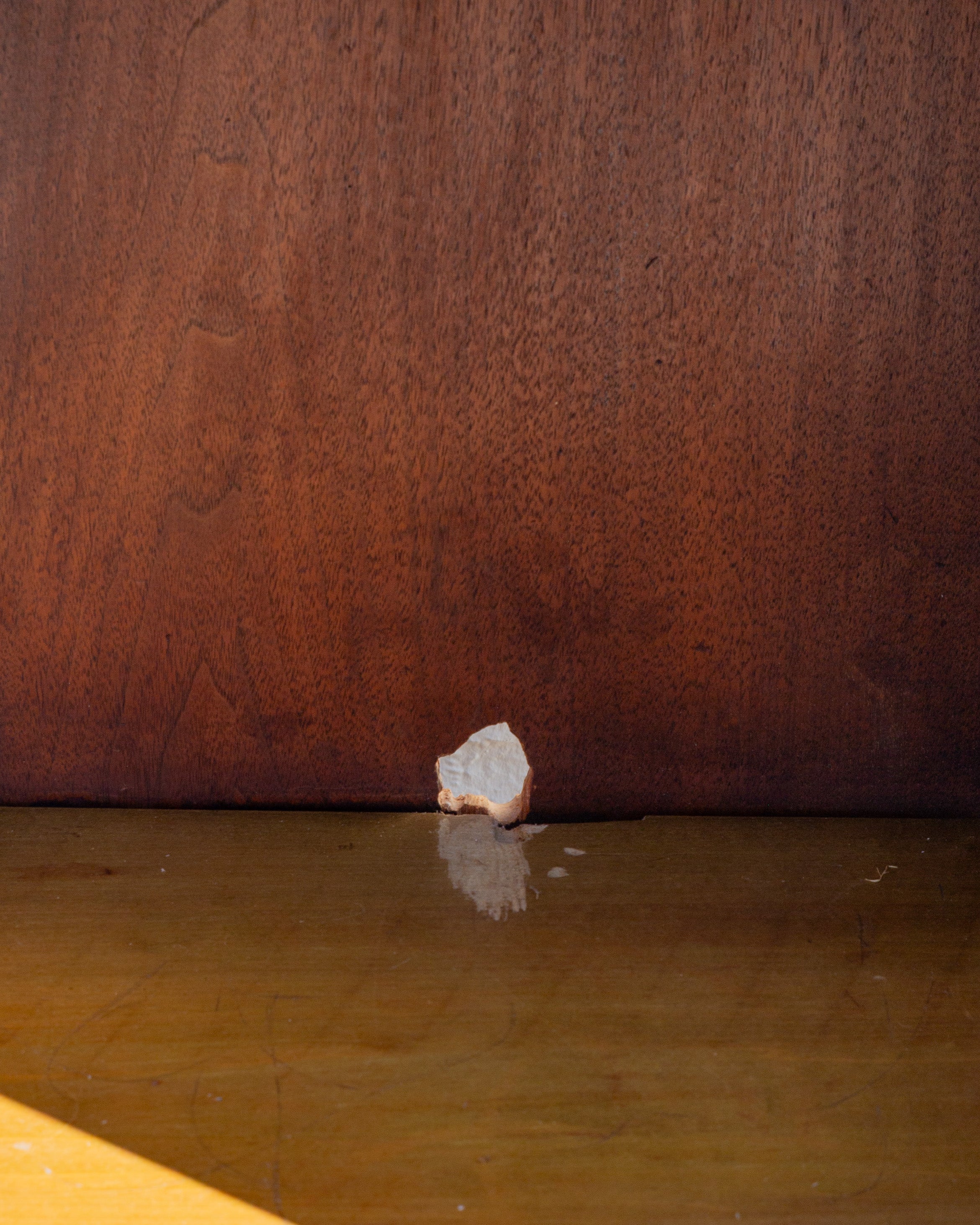 Close detail of a hole through the back panel of the cabinet interior, just above the shelf, with light showing through from behind