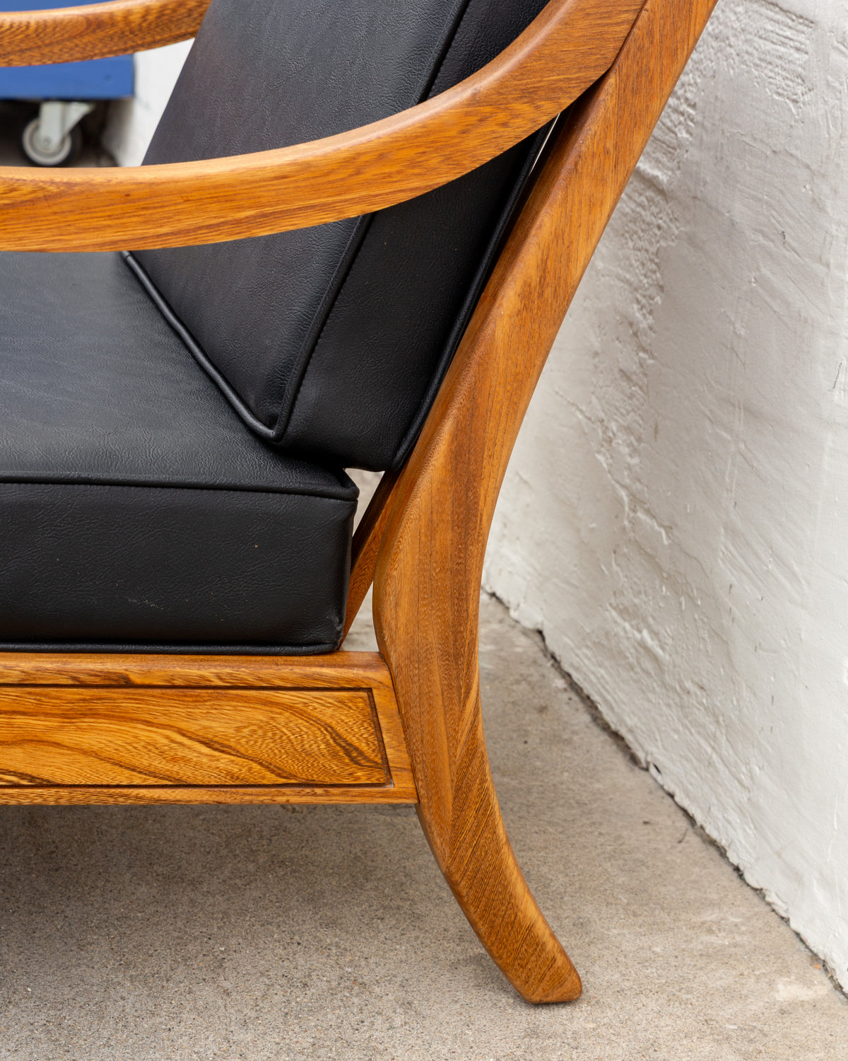 Detail of the curved sabre back leg and sloping arm in golden oak, with black seat and back cushions set in the frame