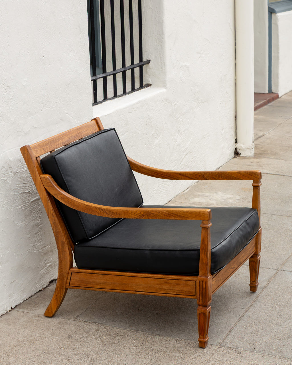 Three-quarter view of a mid century oak arm chair with black cushions against a white stucco wall
