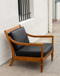 Three-quarter view of a mid century oak arm chair with black cushions against a white stucco wall
