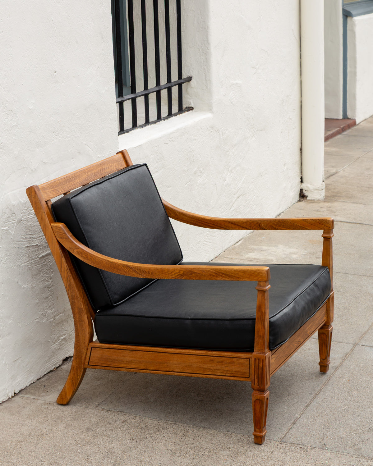 Three-quarter view of a mid century oak arm chair with black cushions against a white stucco wall