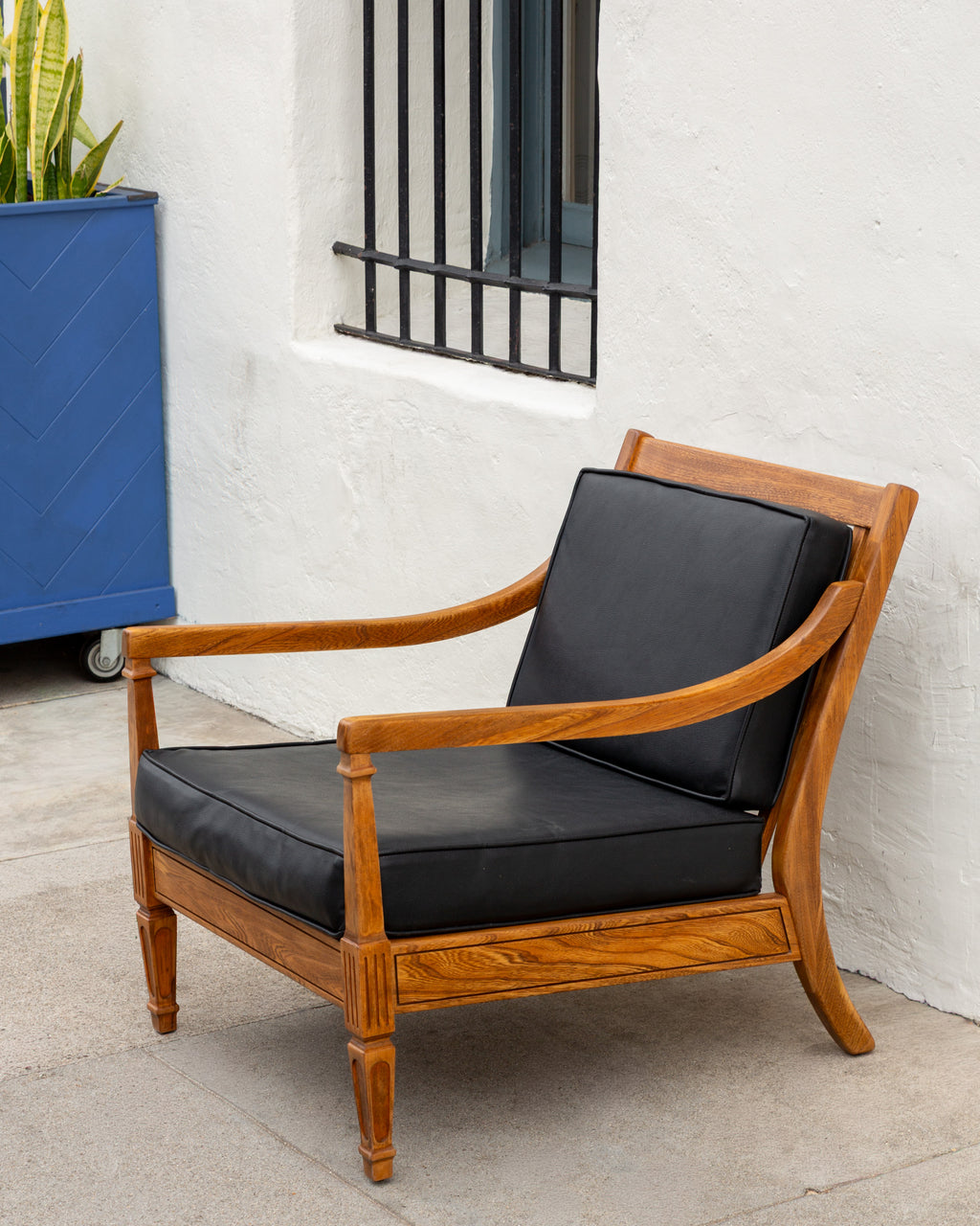 Angled view of the mid century oak arm chair on a sidewalk beside a blue planter and snake plant