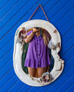 Vintage white ceramic wall mirror on a blue wall, its irregular oval plate reflecting the shop interior.