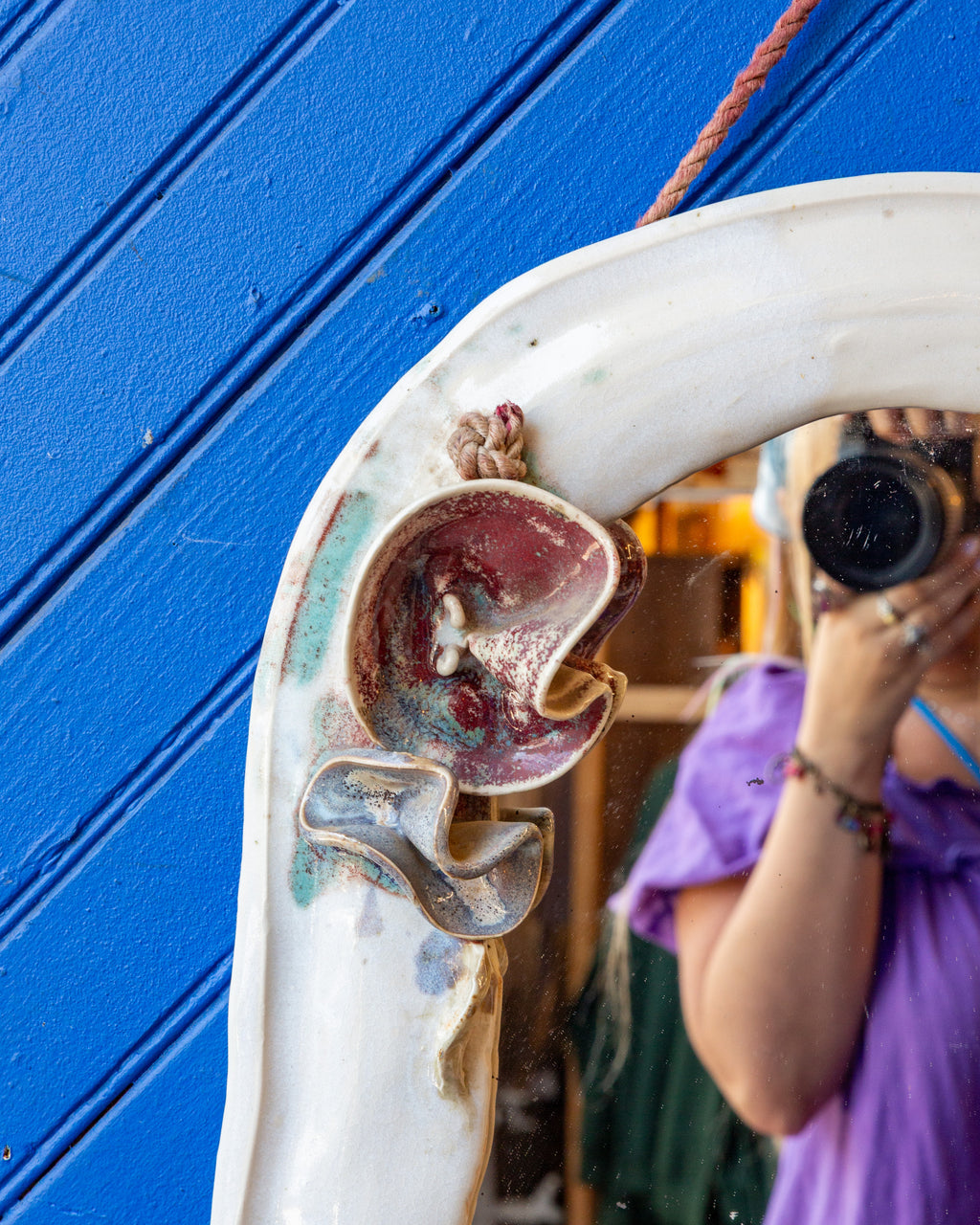 Detail of the upper left corner of the white ceramic mirror, with a deep red glazed flower and knotted hanging cord.