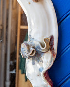 Close detail of a ruffled ceramic blossom in blue and amber glaze on the white mirror frame.