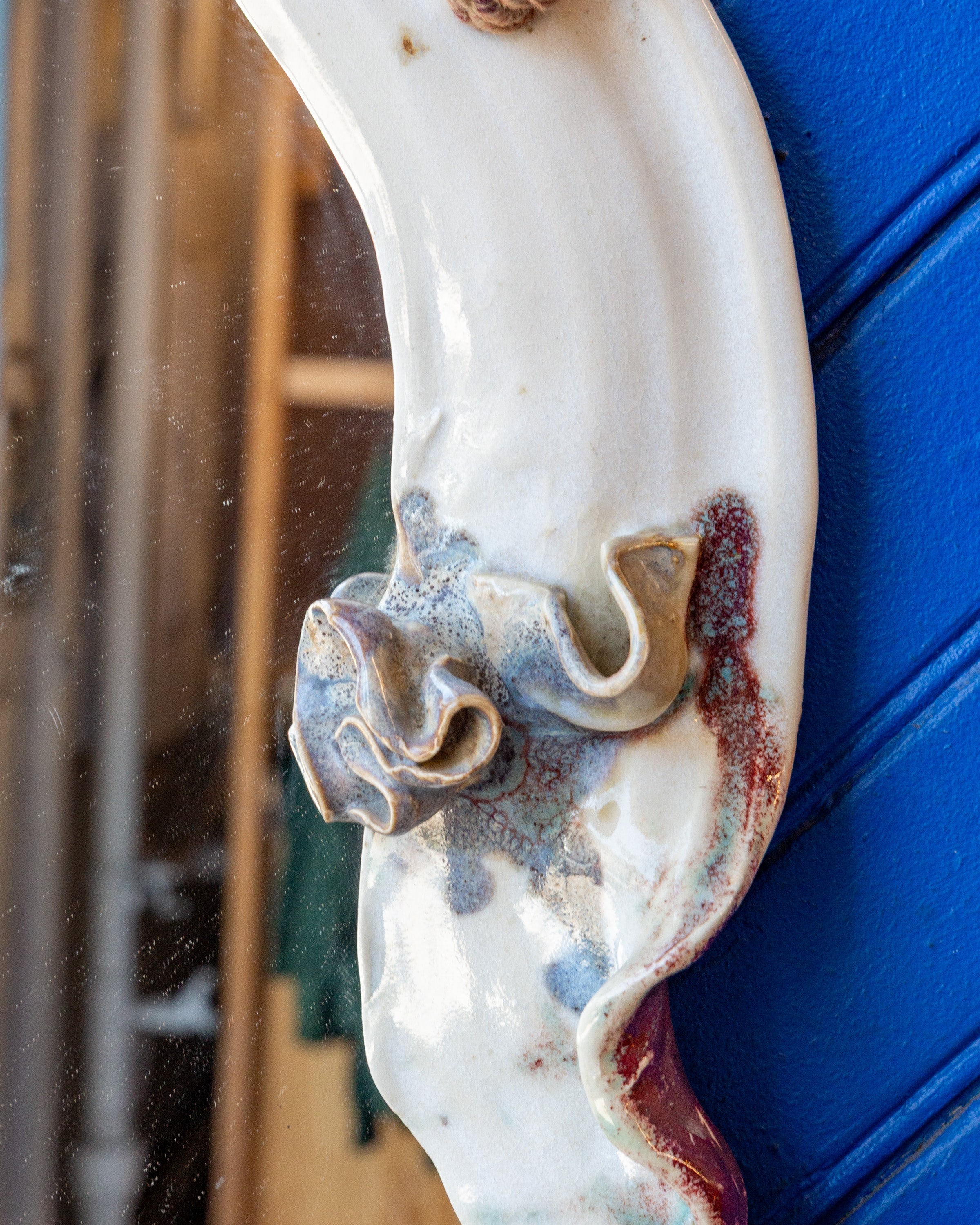 Close detail of a ruffled ceramic blossom in blue and amber glaze on the white mirror frame.