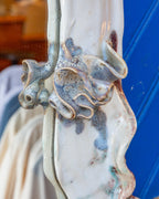Tight detail of ruffled blue and cream ceramic petals applied to the white mirror frame.