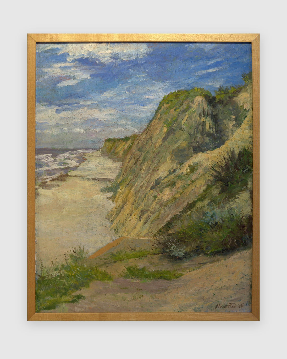 Straight-on view of a John Modesitt painting of a golden coastal bluff and beach near San Diego in a light wood frame, on a light gray background.