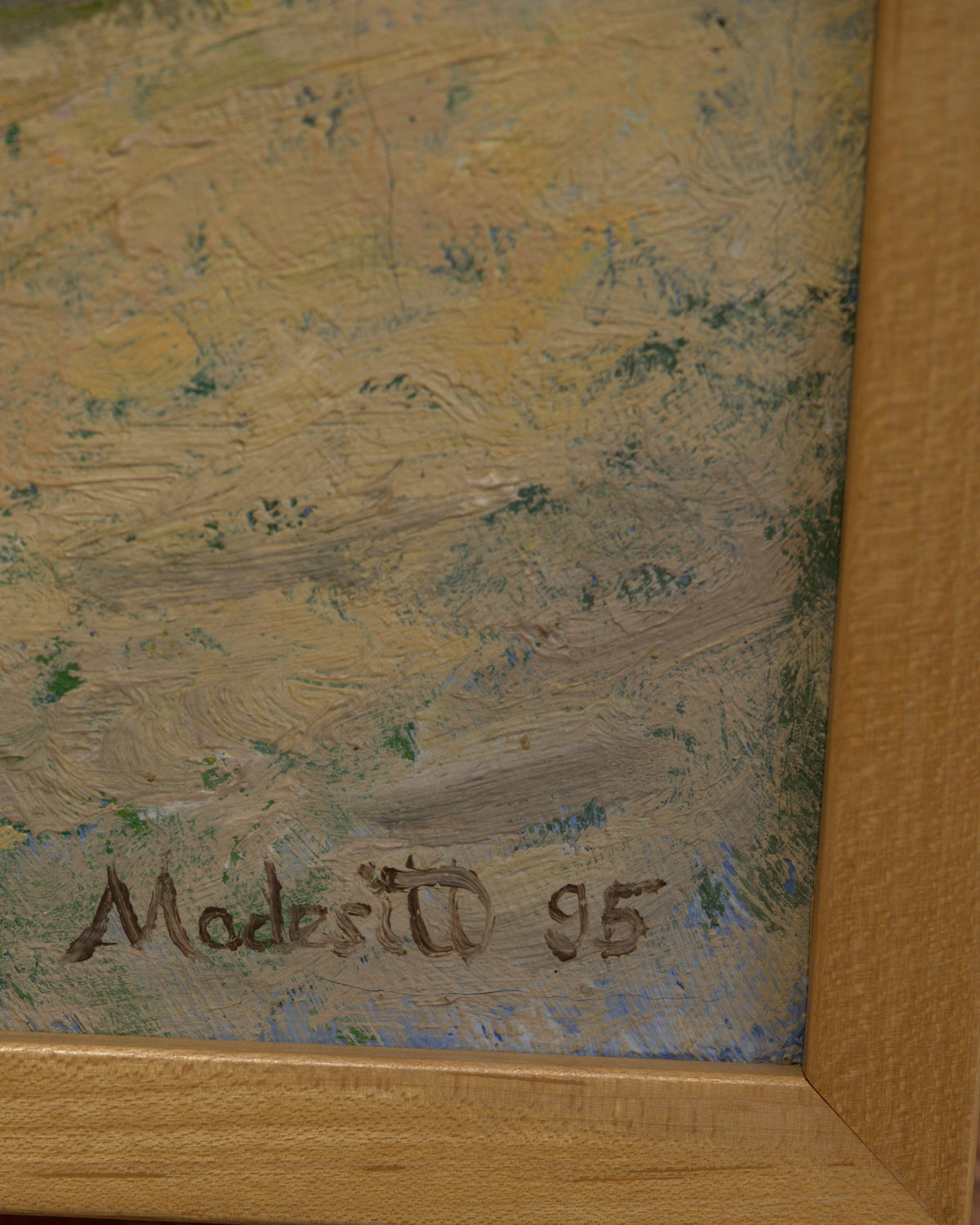 Detail of the Modesitt 95 signature at lower right of the coastal bluff painting, above the light wood frame.
