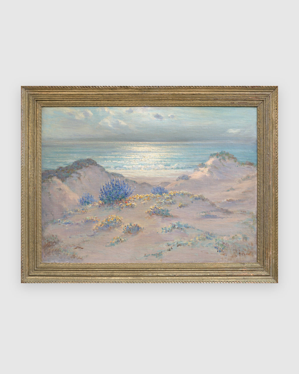 Straight-on view of a Frank Montague Moore painting of sand dunes with blue lupine and a silver sea in a ribbed gilt frame, on a light gray background.