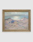 Straight-on view of a Frank Montague Moore painting of sand dunes with blue lupine and a silver sea in a ribbed gilt frame, on a light gray background.