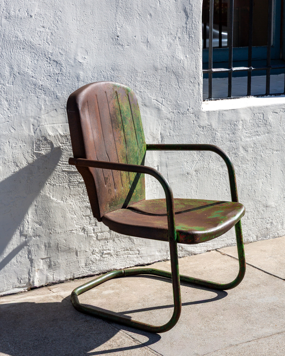 Three-quarter view from the left of a green and rust patinated steel motel chair on a cantilevered tube base