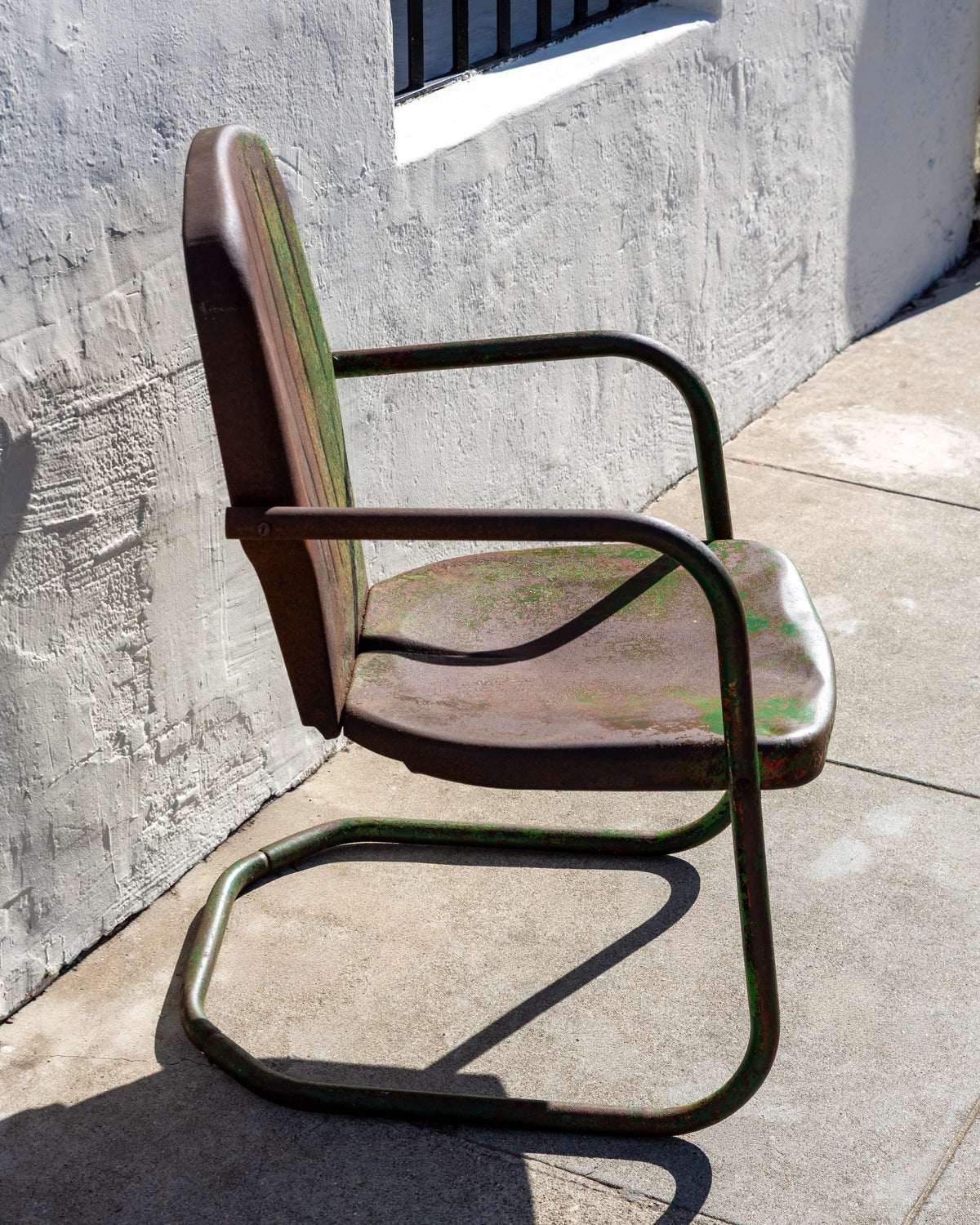 Side profile of a mid century steel motel chair showing the looped cantilever base and curved tubular arm