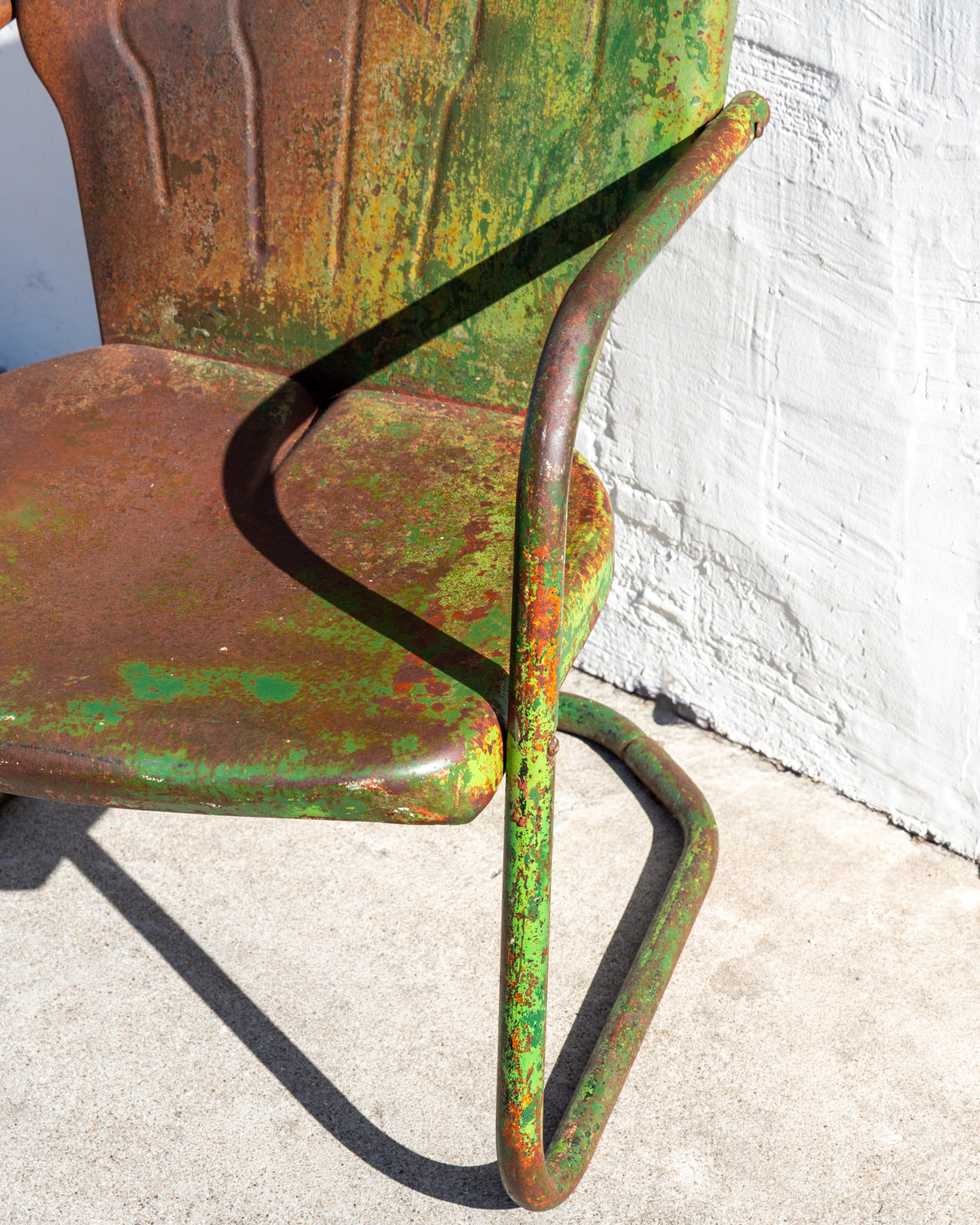 Close view of the dished steel seat and front tube leg of a motel chair with worn green paint over rust